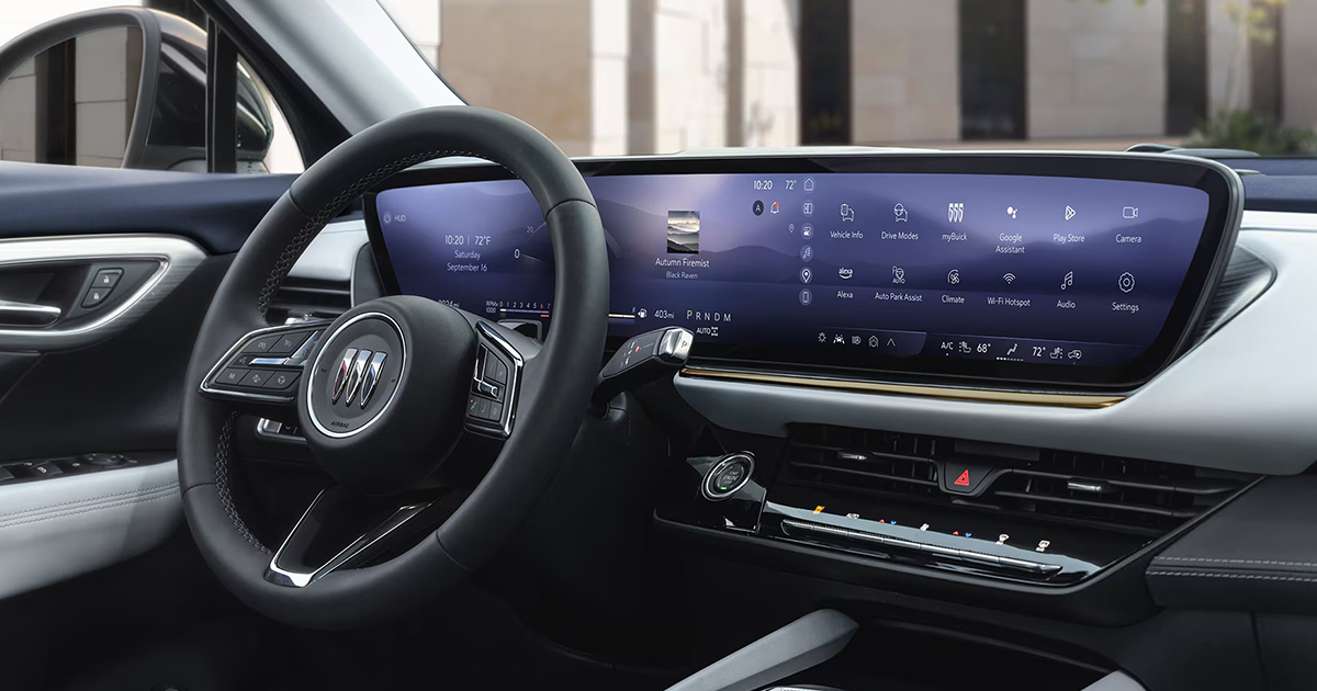 Interior view of a Buick vehicle showing the steering wheel with Buick logo and a wide digital display dashboard featuring navigation, media, climate, and vehicle controls.