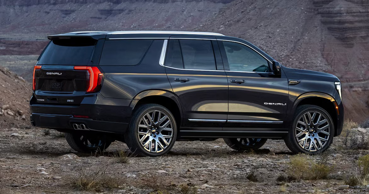 Black GMC Yukon Denali parked outdoors against a rocky canyon backdrop, showcasing its large chrome wheels, bold styling, and Denali badging.