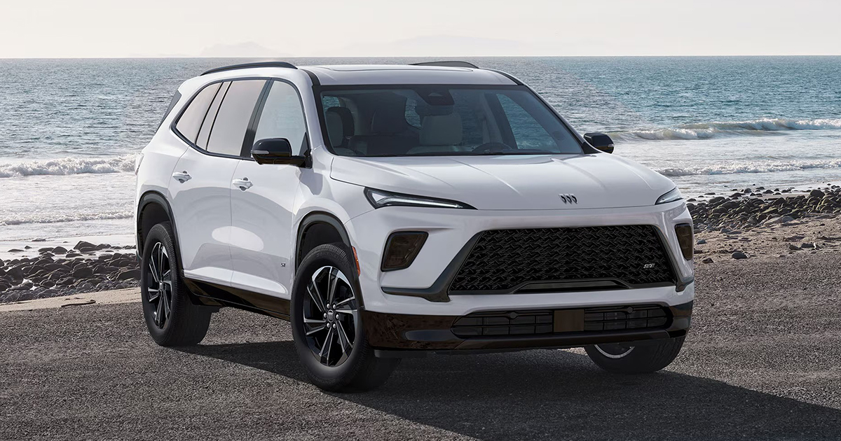 White Buick Enclave parked on a coastal road with waves in the background, highlighting its modern front grille and sporty styling.